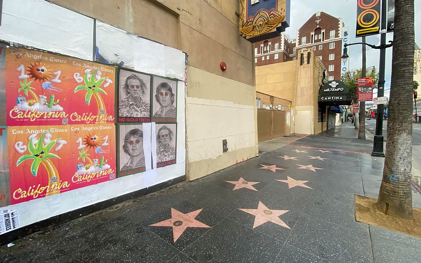 California 101 posters wheatpasted on a white-papered wall along the Hollywood Walk of Fame, with pink terrazzo stars running down the sidewalk